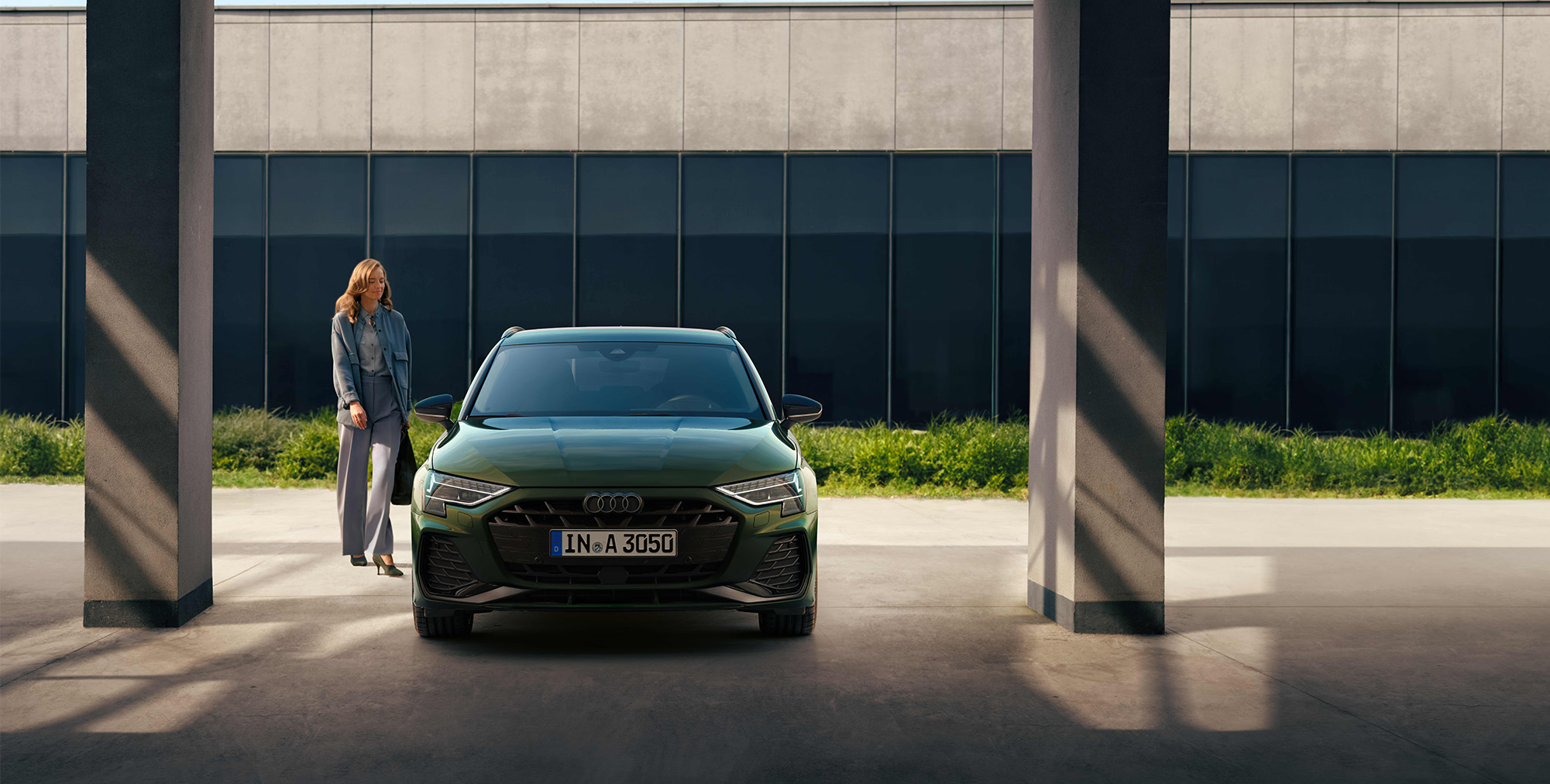 Ein gr&uuml;ner Audi A3 Sportback in der Frontansicht, mit einer auf das Fahrzeug zugehende Frau