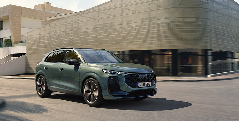 gr&uuml;ner Audi Q3 f&auml;hrt auf Stra&szlig;e vor Geb&auml;ude