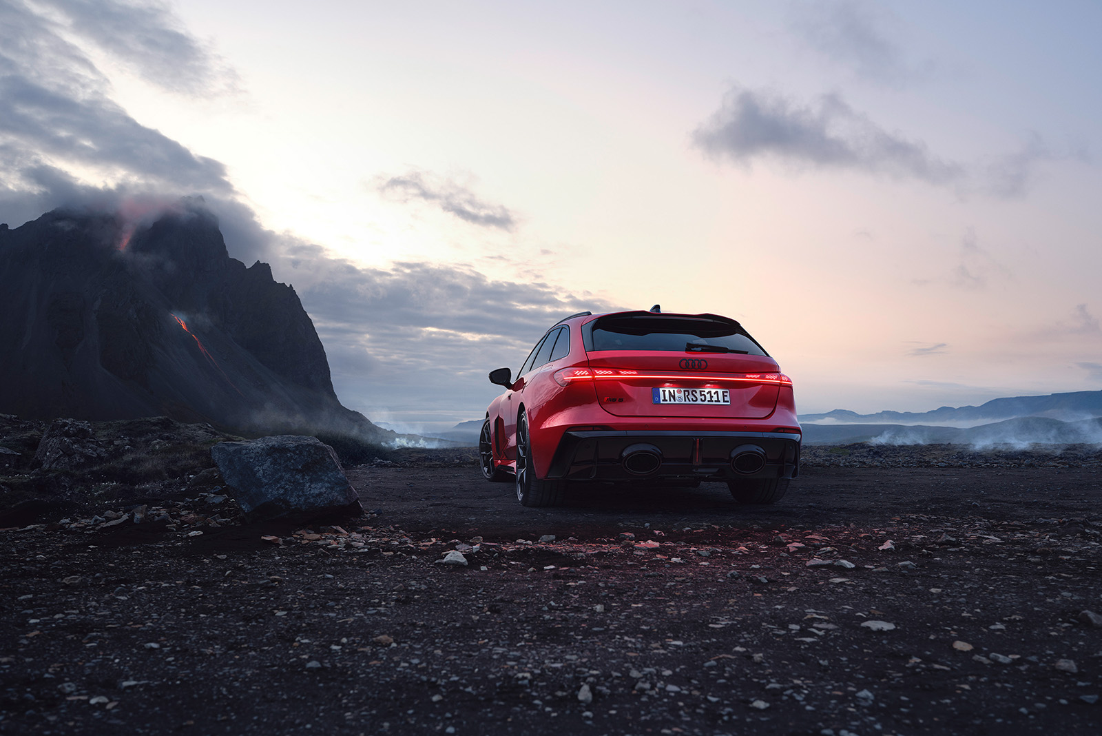 Audi RS 5 Avant, rot, Heckansicht, auf dunklem Steinboden mit Bergen links im Bild